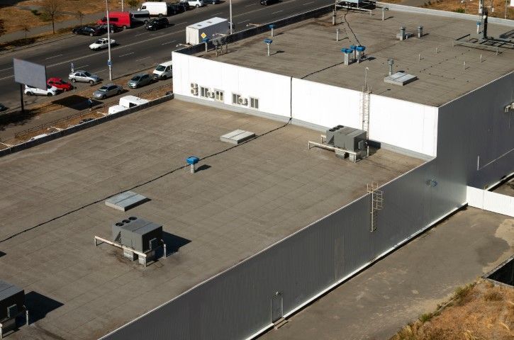 Aerial view of a flat-roofed industrial building with HVAC units and a parking lot nearby