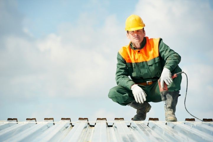 Construction worker in safety gear crouching on a metal rooftop, inspecting the surface with a cable in hand.