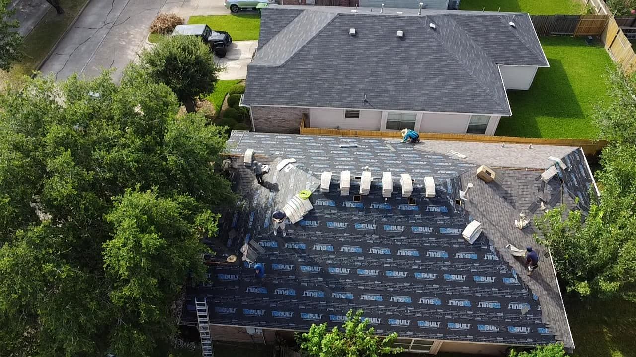 Aerial view of workers installing black underlayment on a residential roof during a construction project.
