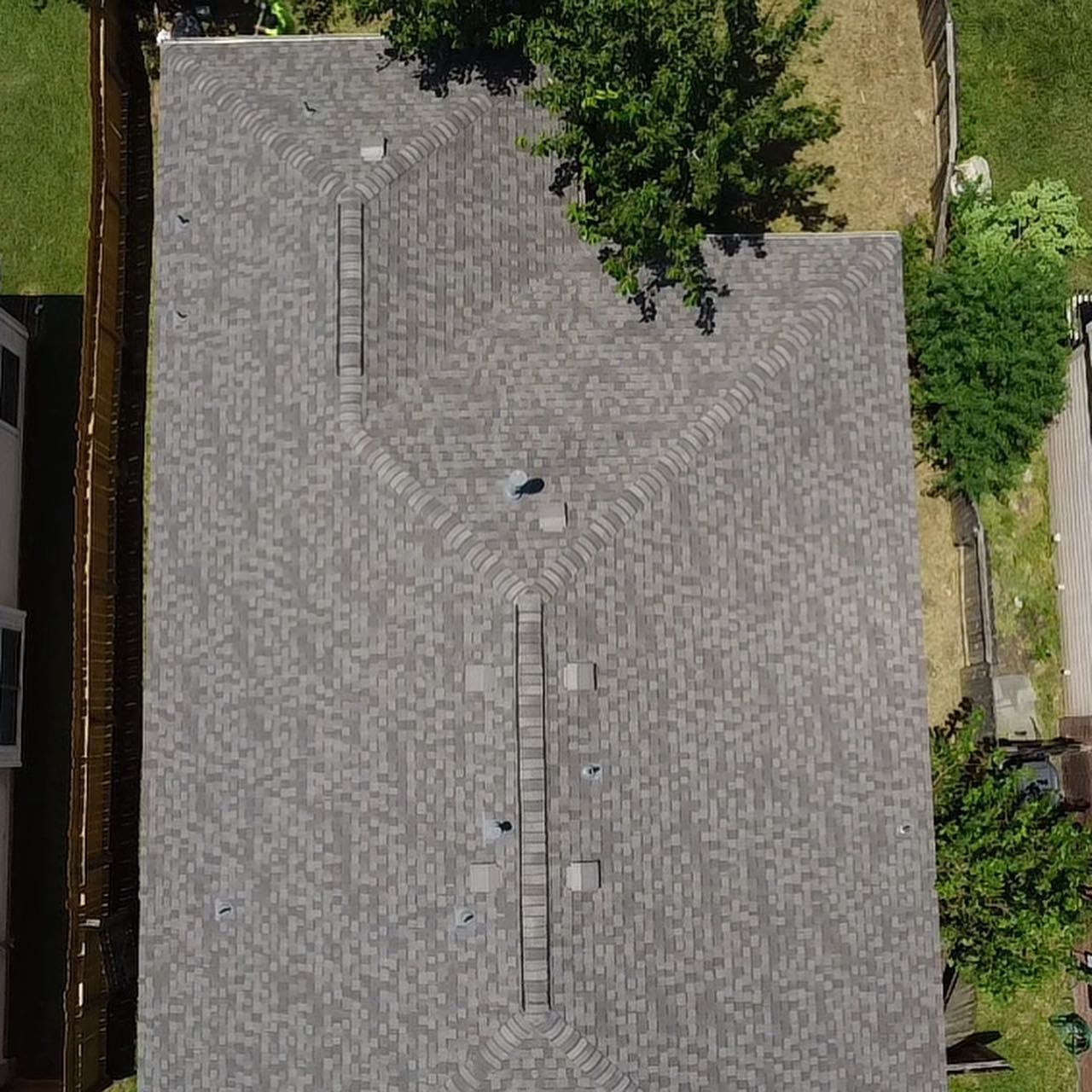 An aerial view of a gray, asphalt-shingled residential roof with several vents, plumbing stacks, and a ladder placed on it.