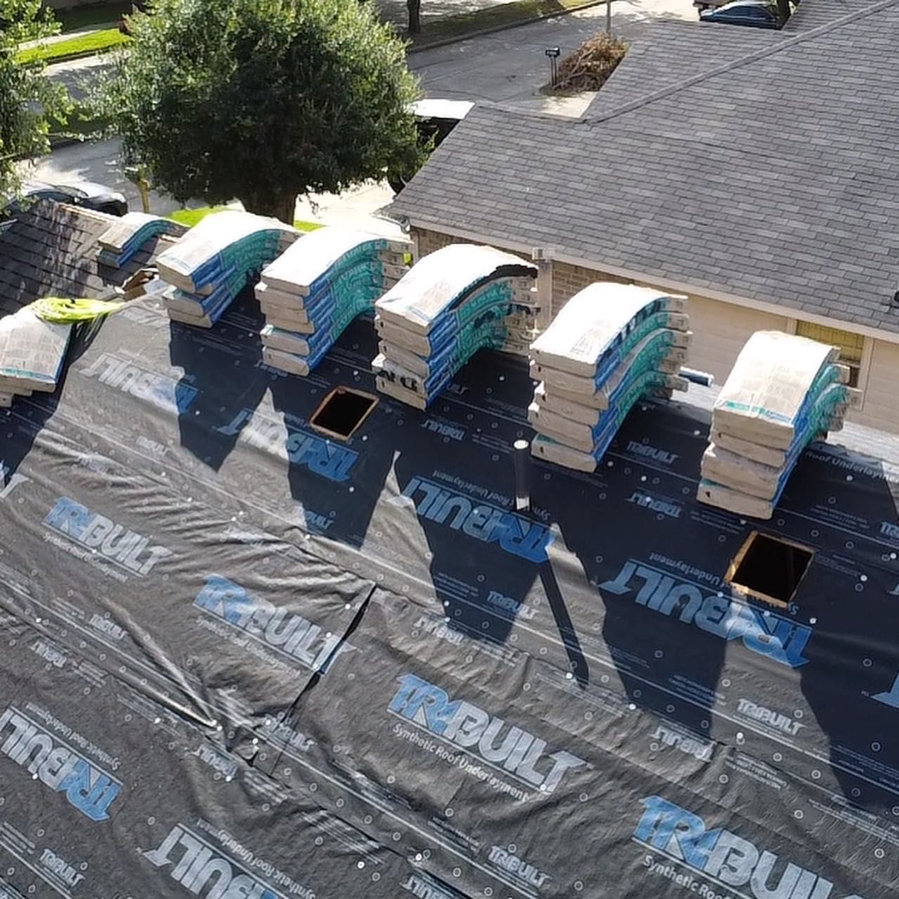 High-angle view of a residential roof under construction, featuring stacks of shingles over black roofing underlayment.