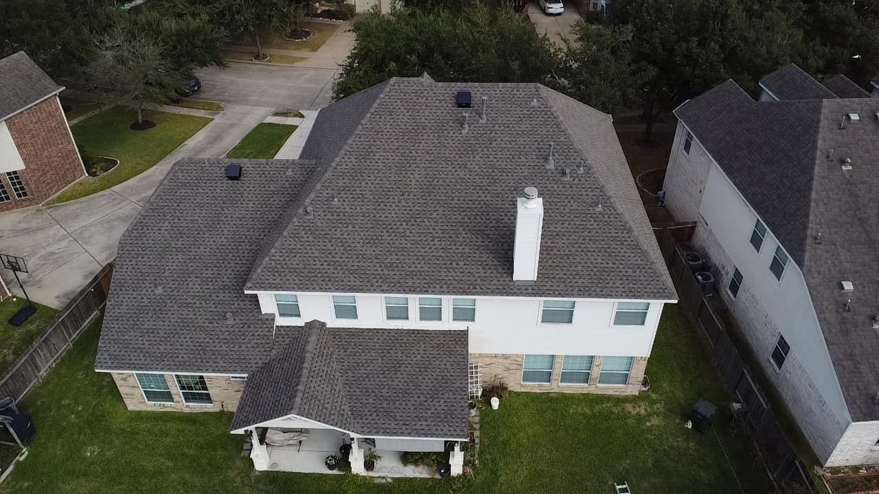 An aerial view of a two-story residential house with a dark shingle roof, white siding, and a chimney.
