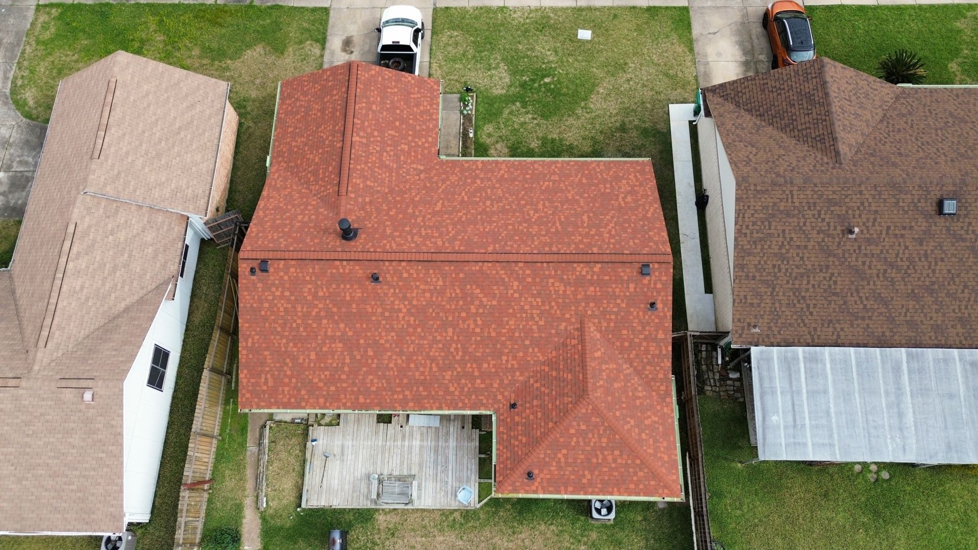A top-down aerial view of three residential homes with shingled roofs, featuring a central house with a red roof.