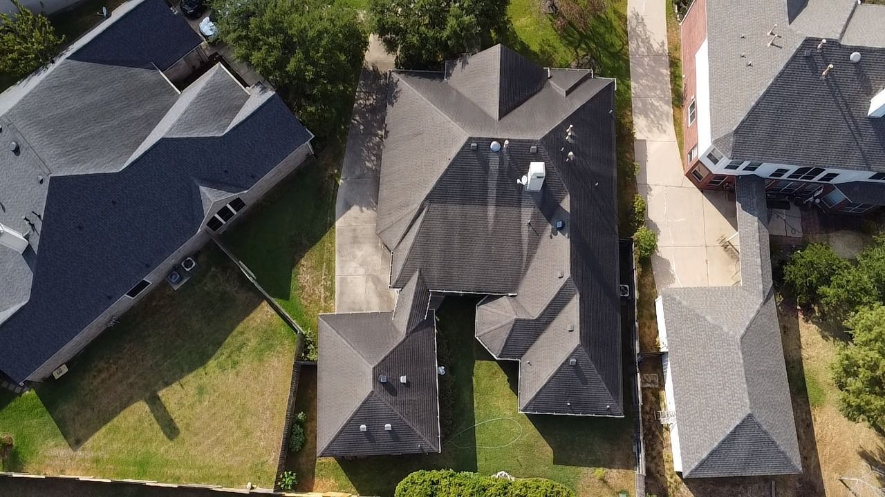 Aerial view of a residential neighborhood showing multiple houses with dark gray roofs and surrounding green lawns.