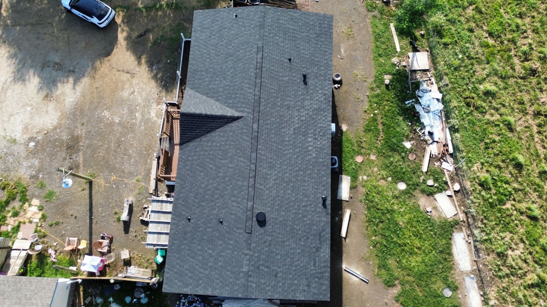 An aerial view of a rectangular house with a grey shingled roof, surrounded by a yard with gravel and green grass.