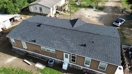 Aerial view of a residential manufactured home with a gray shingle roof, tan siding, and a white back door.