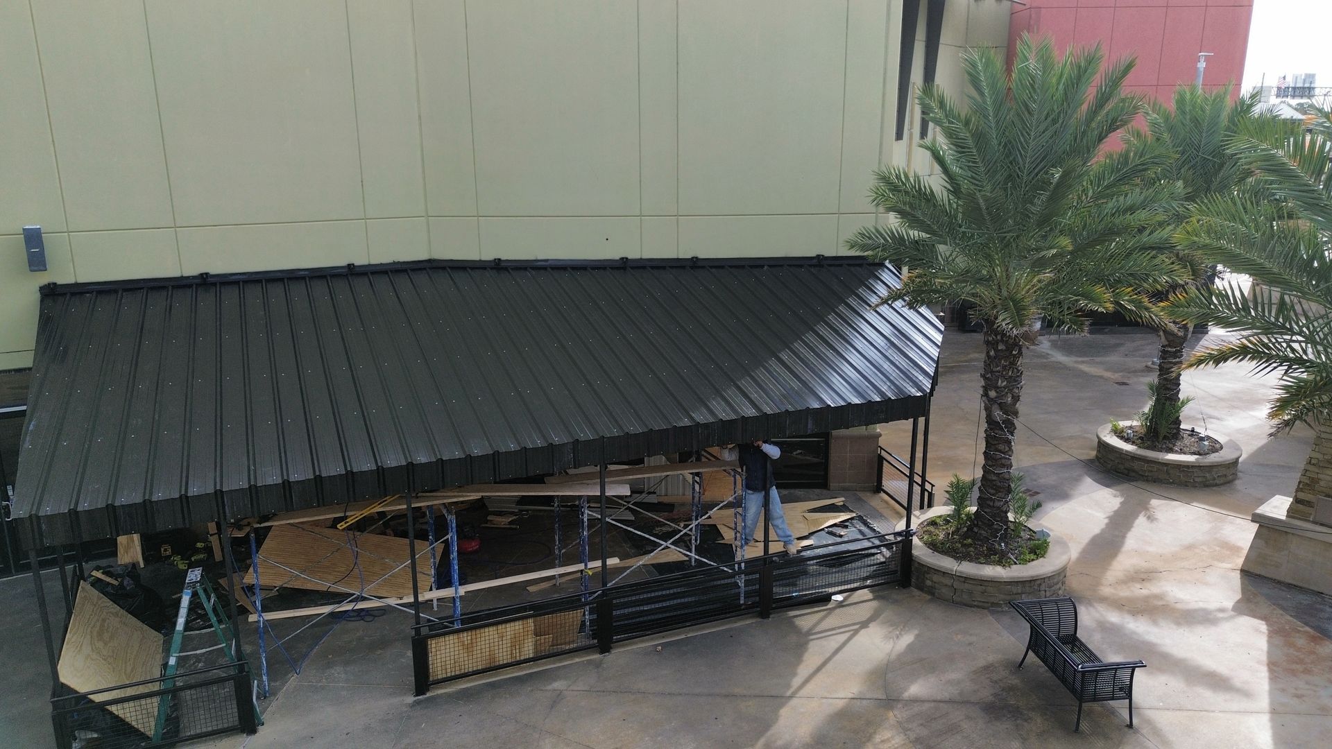 An aerial view of a house roof undergoing renovation with workers removing old shingles to expose the wooden deck.