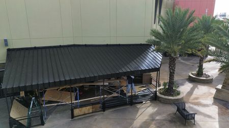 An aerial view of a house roof undergoing renovation with workers removing old shingles to expose the wooden deck.