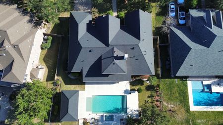 Aerial view of a residential manufactured home with a gray shingle roof, tan siding, and a white back door.