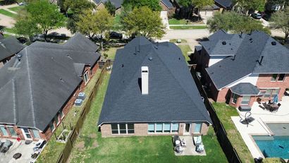 An aerial view of a house roof undergoing renovation with workers removing old shingles to expose the wooden deck.