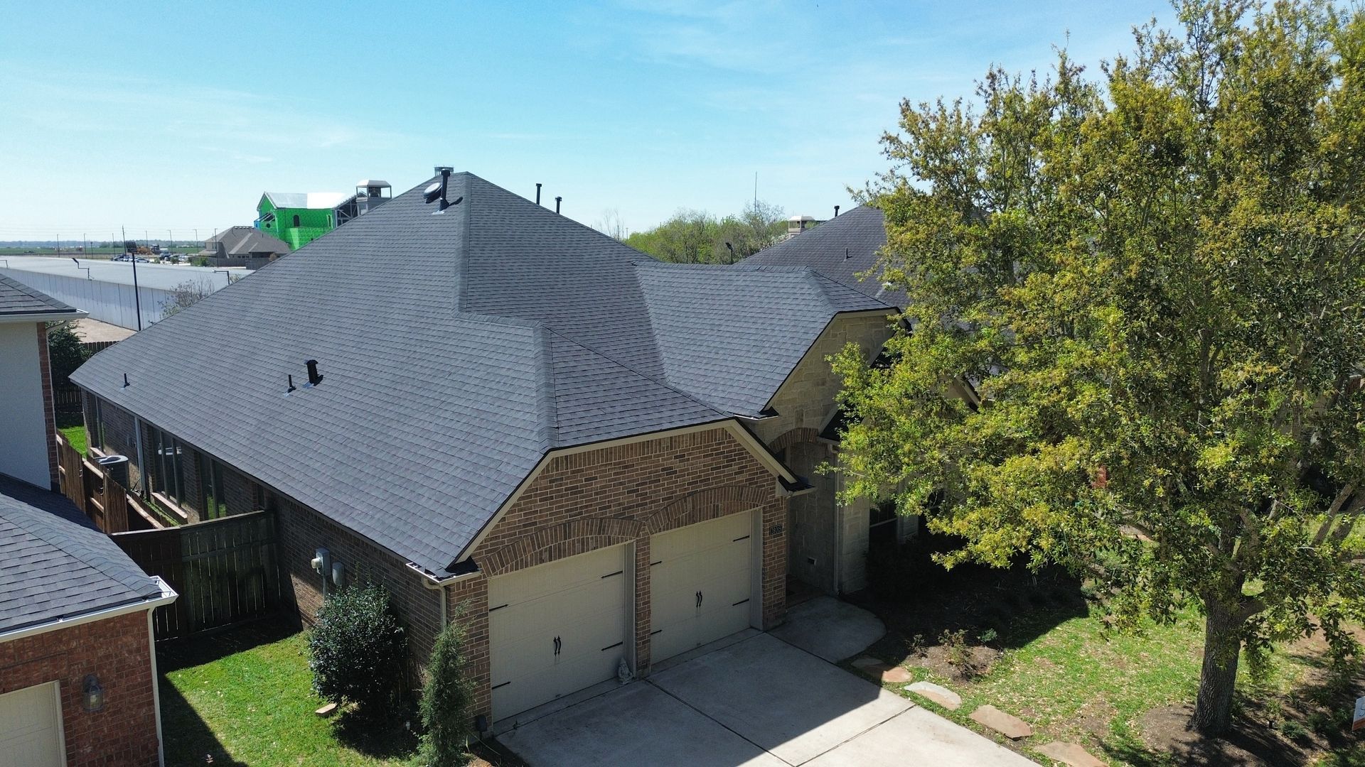 Workers remove old shingles and install new underlayment on a residential roof in a suburban neighborhood.