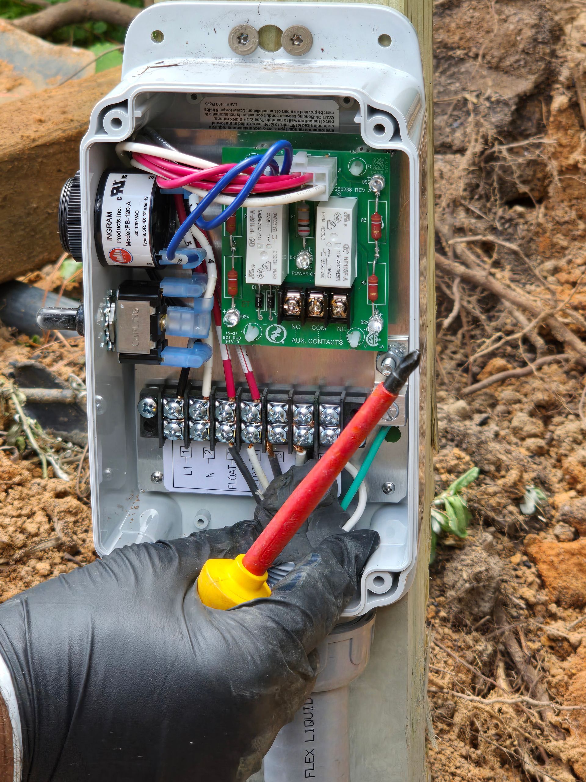 Person in black gloves using a screwdriver on an electrical control box mounted on a pole outdoors.