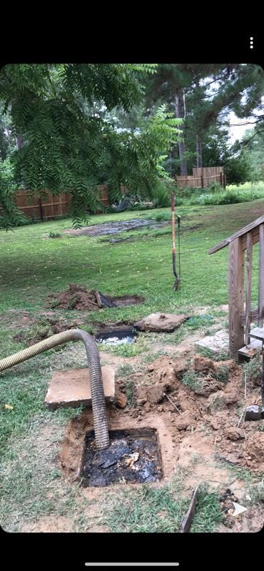 A septic tank being pumped in a grassy yard. A hose extends into the opened tank. Shovel in the background.