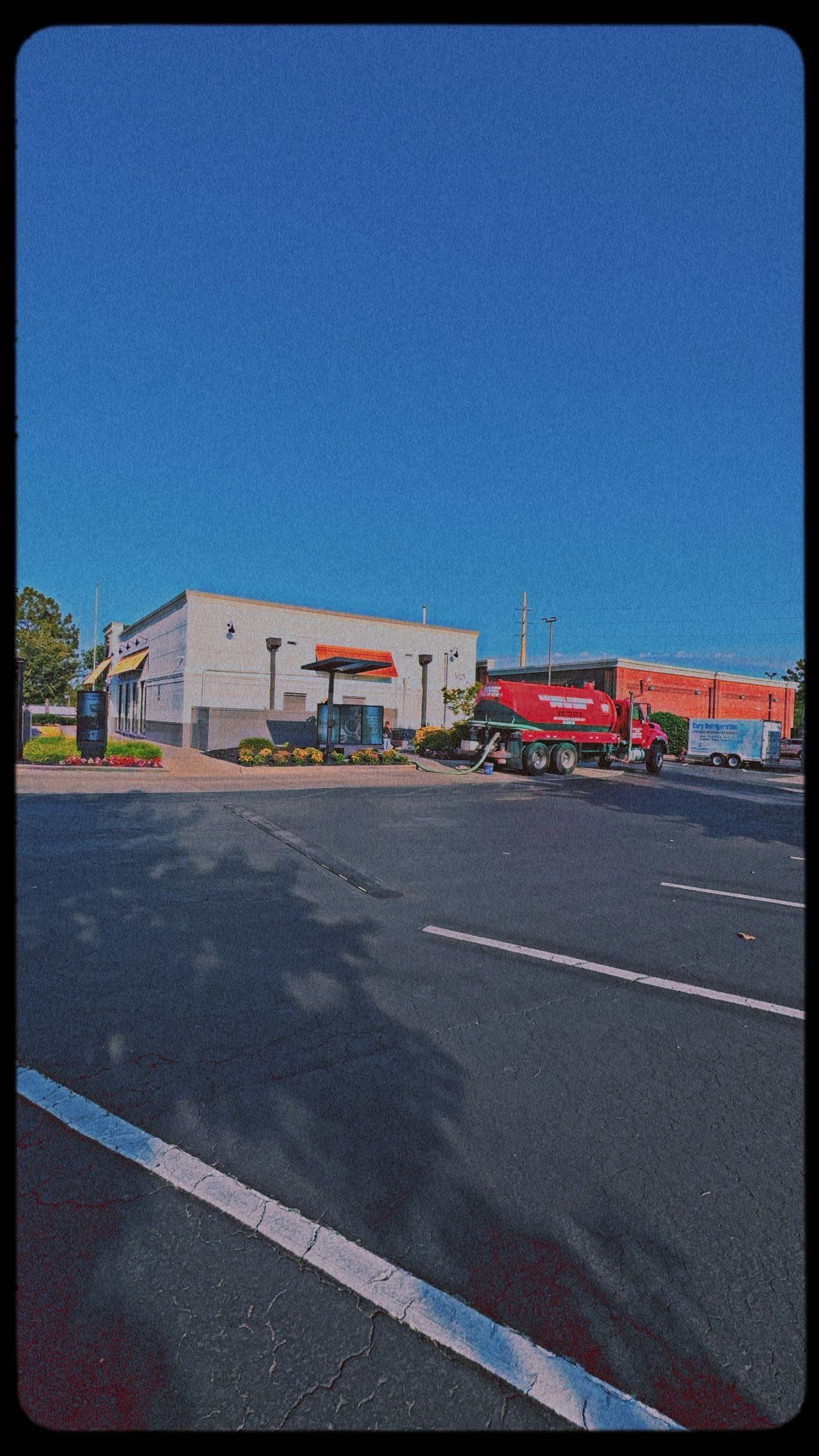 Empty parking lot with a red truck and a white building under a blue sky.