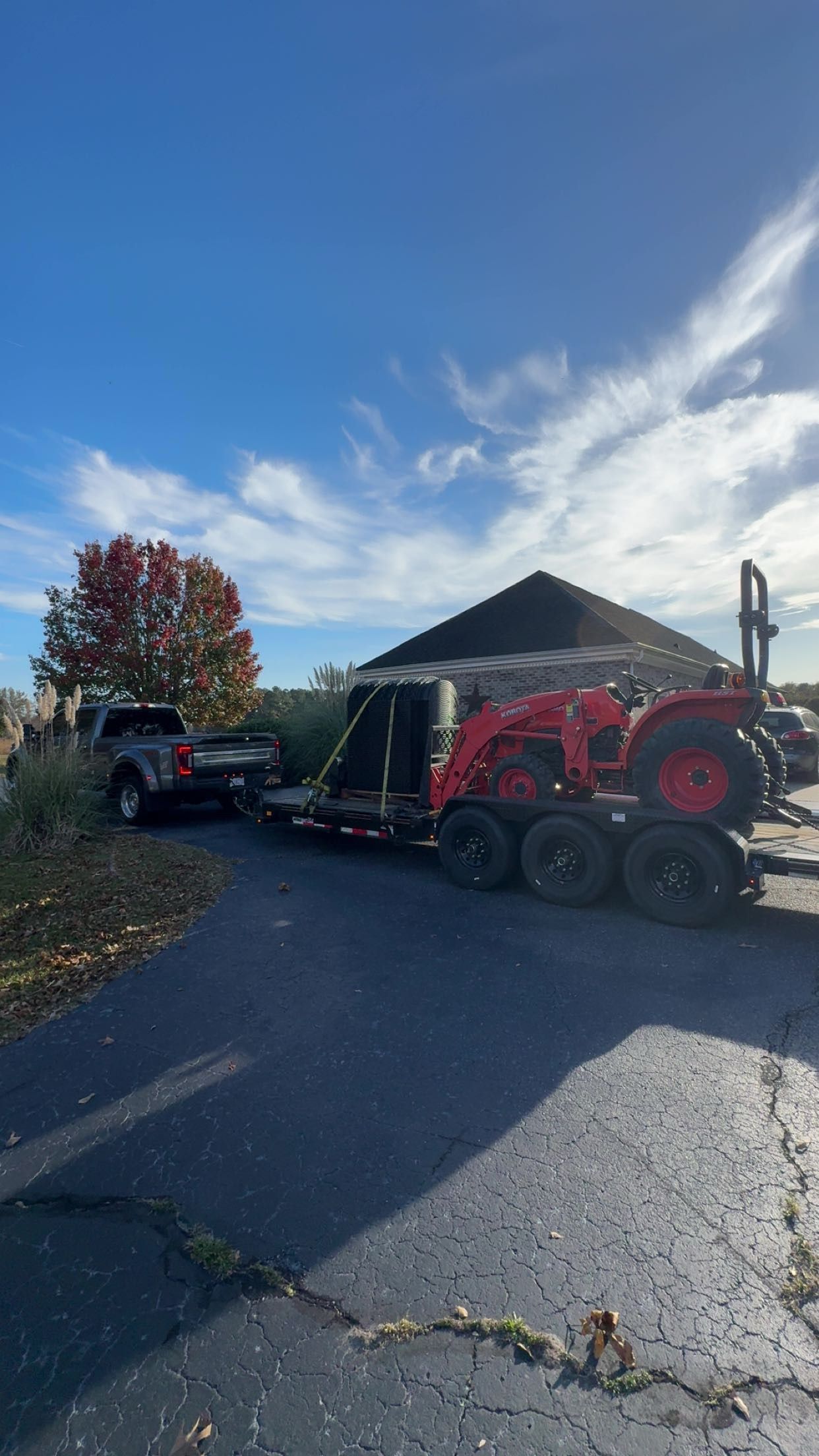 Truck towing a trailer with a red tractor parked on asphalt, under a blue sky.