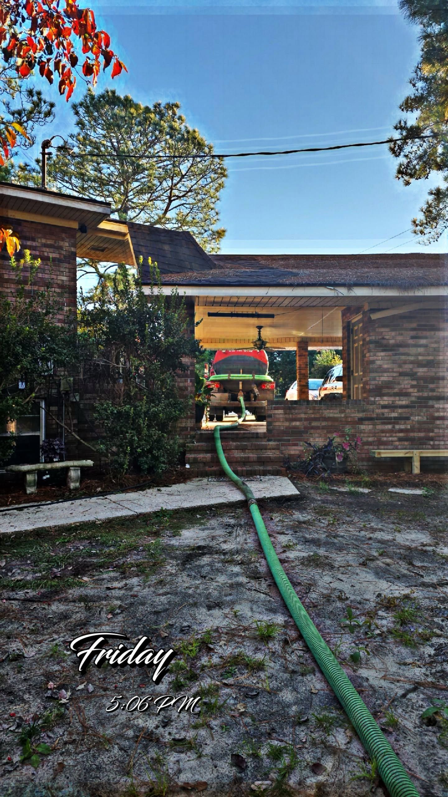 A building with a green hose, person inside window with a sunny sky and trees in the background.