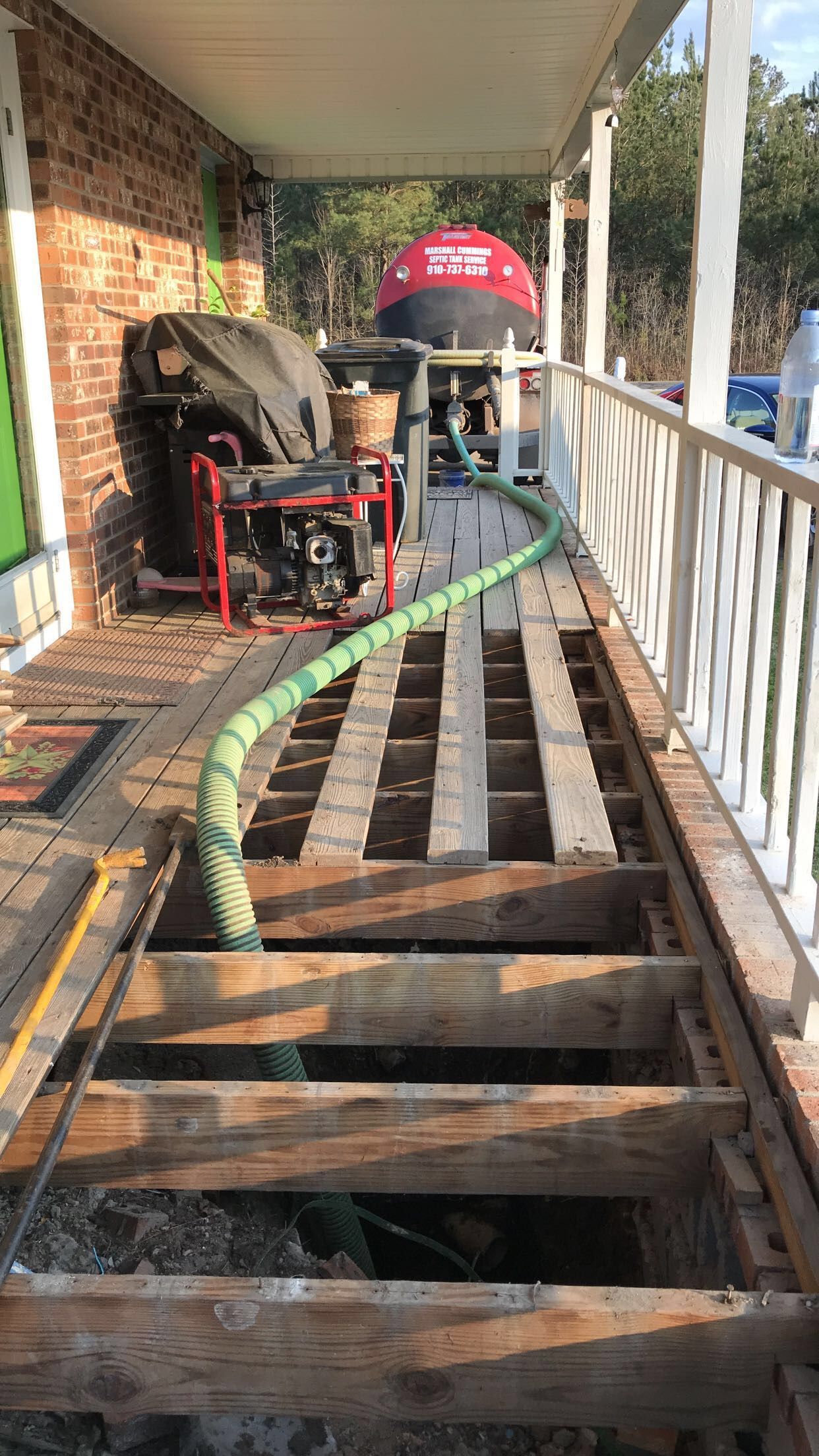 Porch floor being replaced; exposed beams, hose connected to equipment, house exterior.