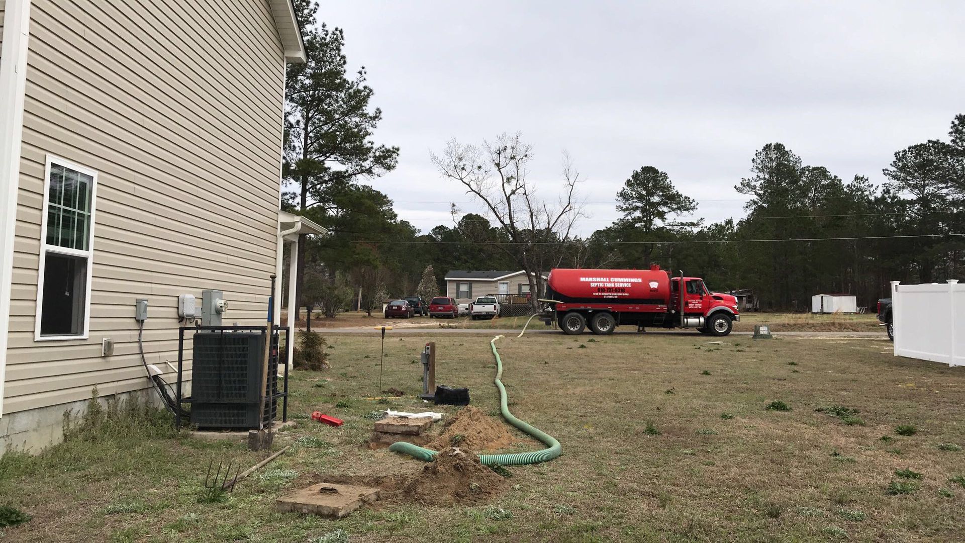 Septic tank pumping service: Red truck with hose in a yard next to a house.