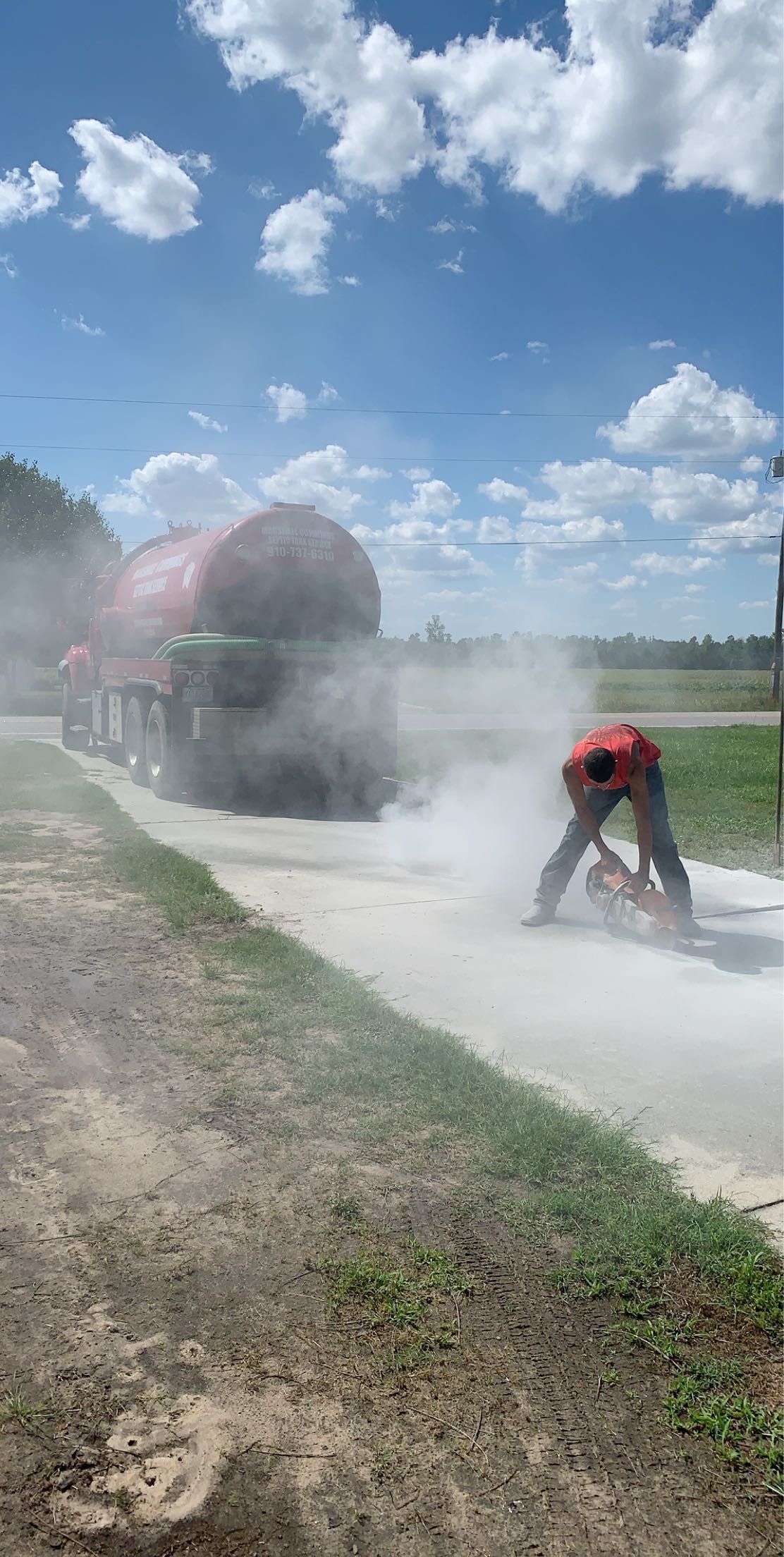 Person cutting concrete in front of a truck loaded with hay bales on a sunny day.