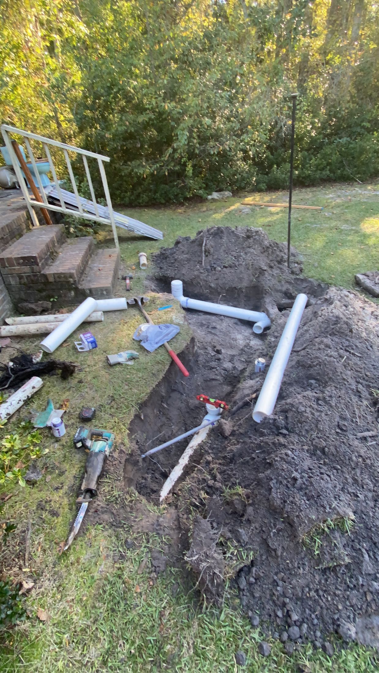 Outdoor plumbing repair site with exposed pipes and dirt pile near a porch.