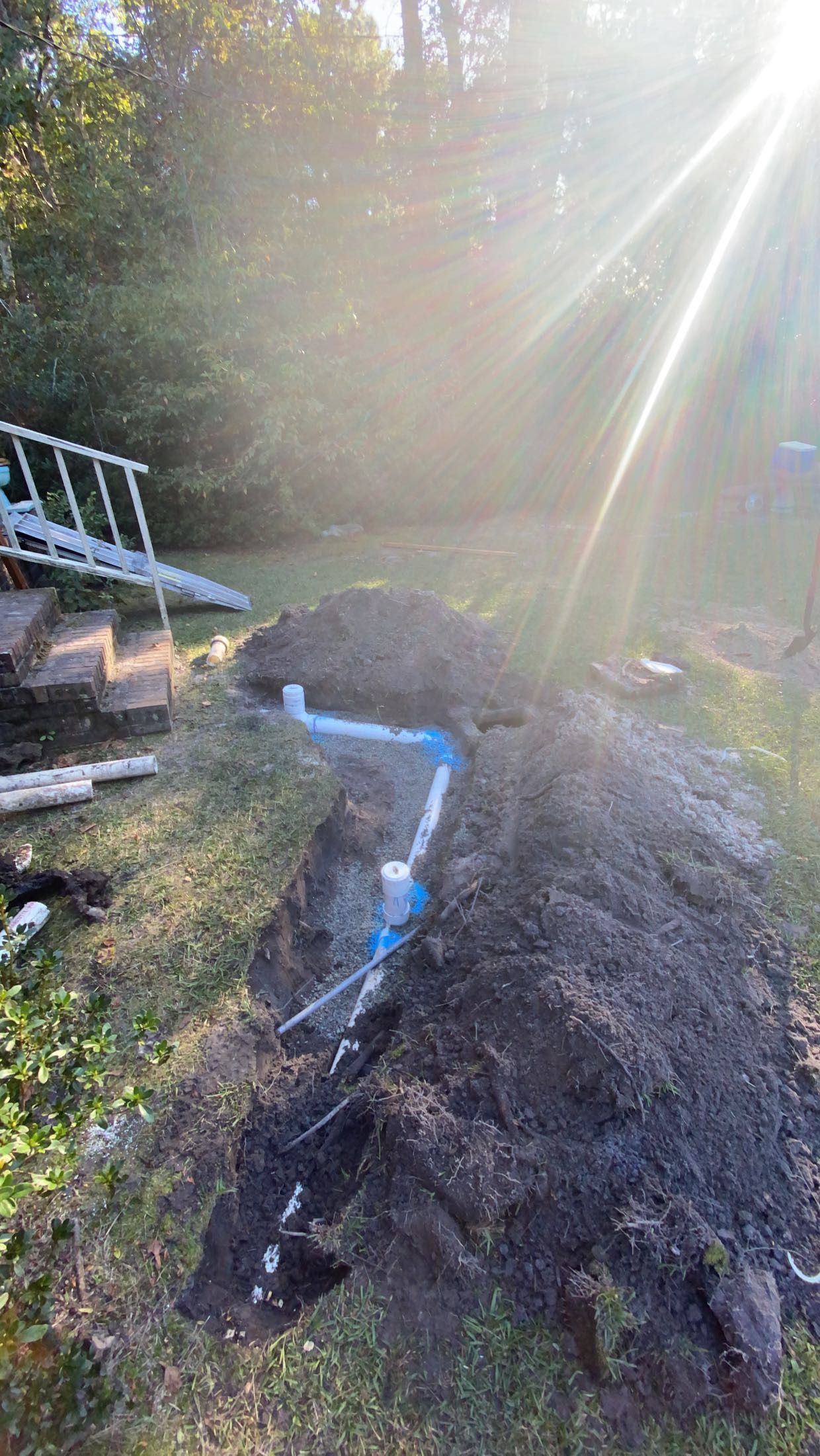 Blue water pipes exposed in a pile of dirt, sunlight shining from the top right.