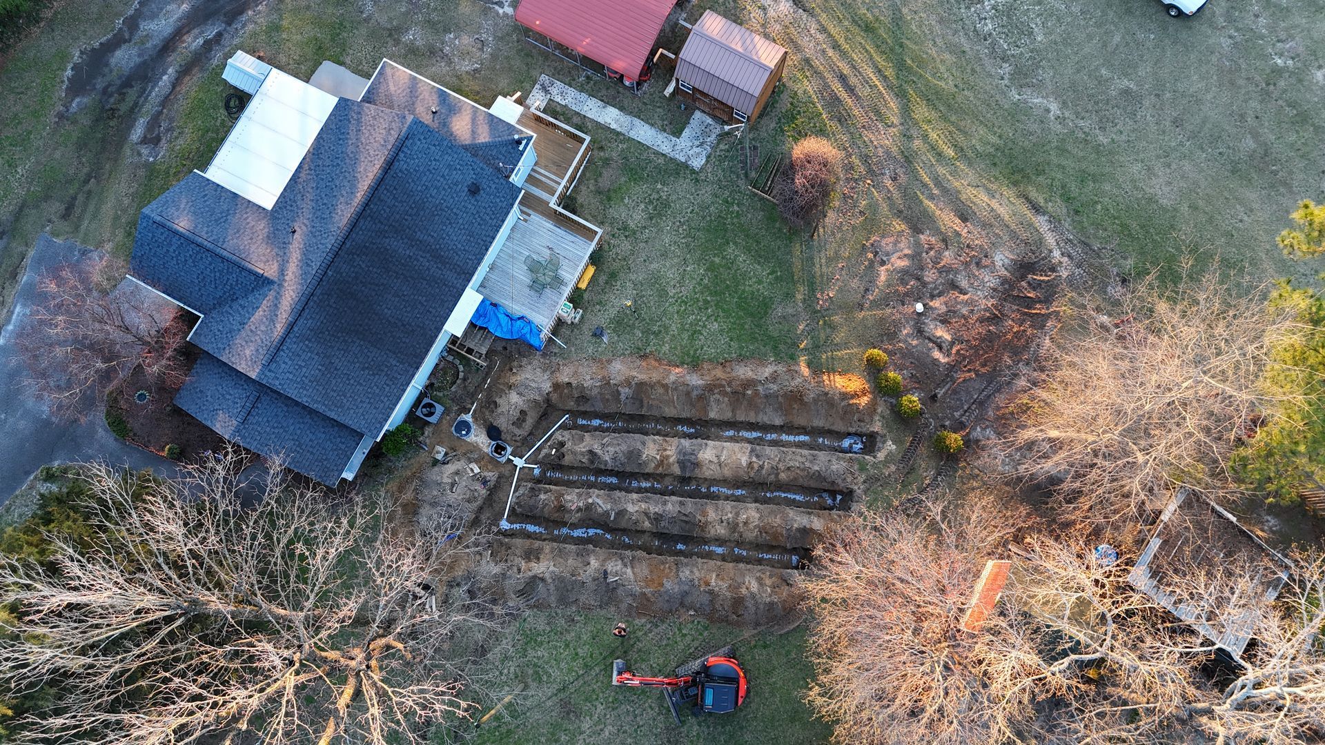 Aerial view: House with dark roof, three garden beds being prepped in yard; small excavator.