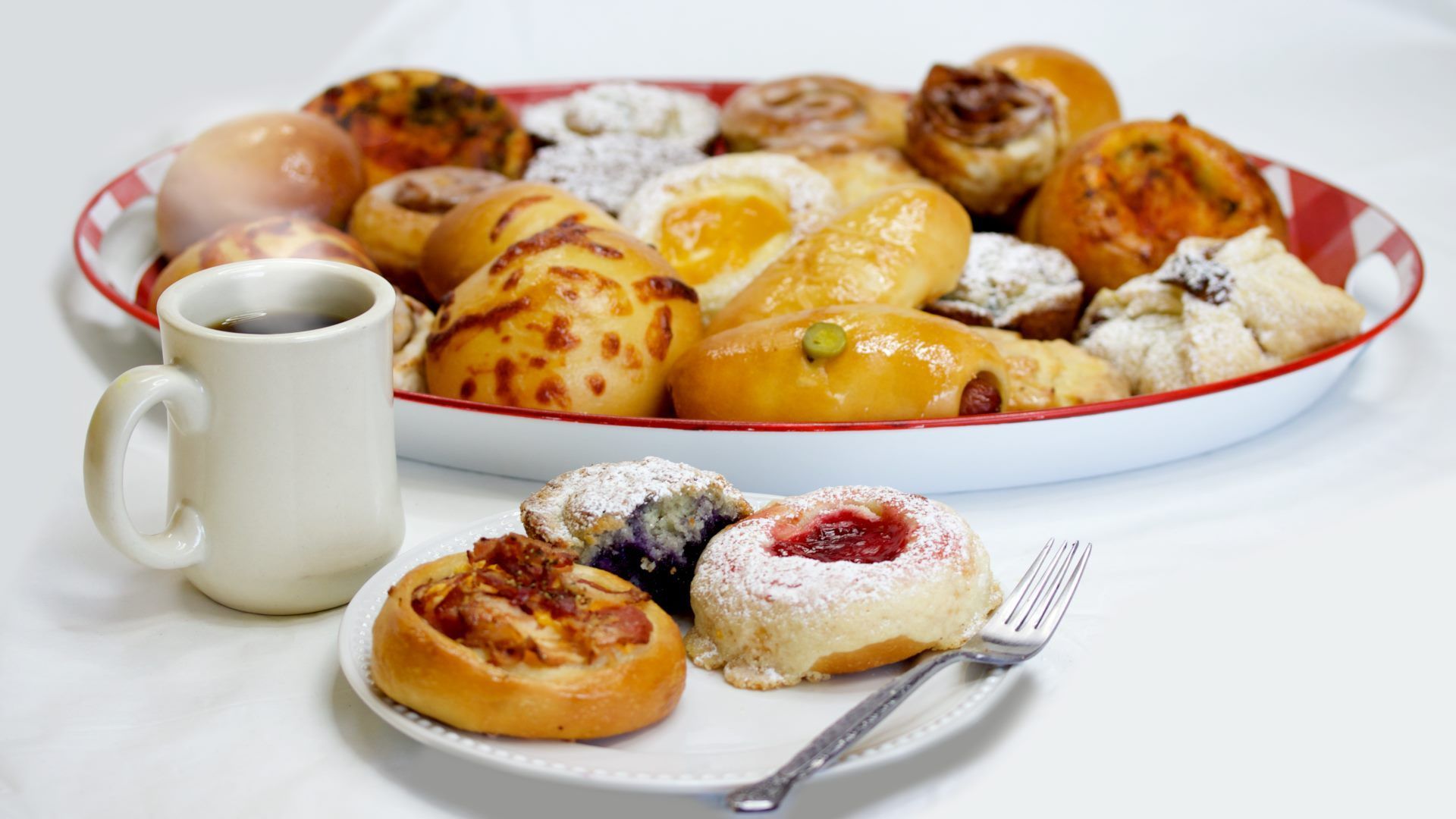 Plate of assorted pastries and a cup of coffee, featuring jam-filled, powdered, and golden baked goods.