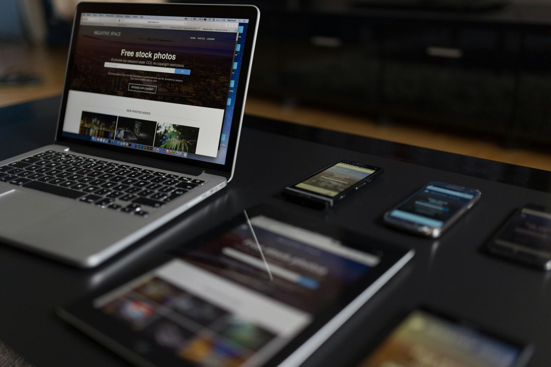 A laptop is open on a table next to a tablet and phone