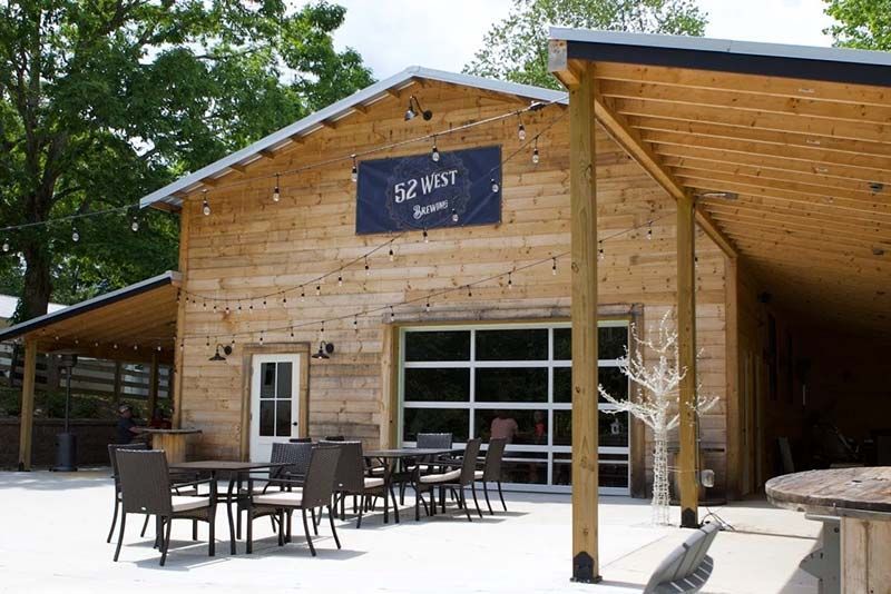 Wooden building with outdoor patio tables and chairs under a slanted roof, sign reading “52°58” above the entrance