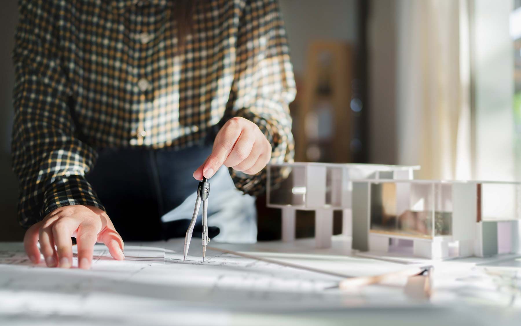 Person using a compass over architectural plans beside a scale building model
