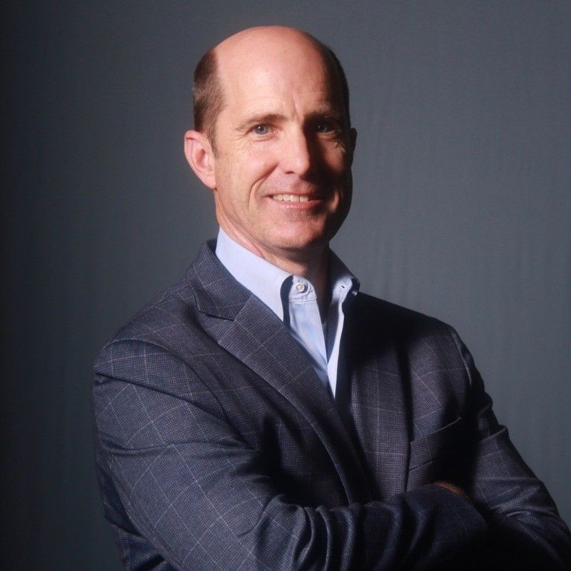 Smiling man in a gray suit with arms crossed against a dark background