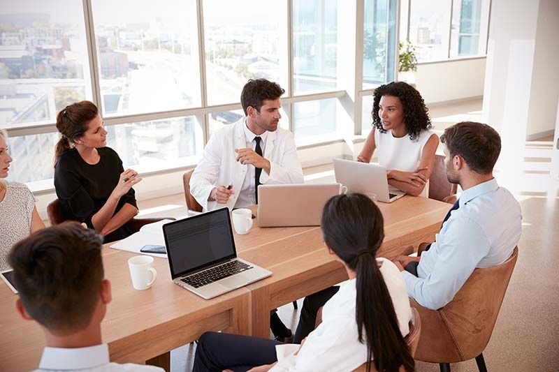 Team meeting around a wooden table in a bright office, with a laptop and papers in use.