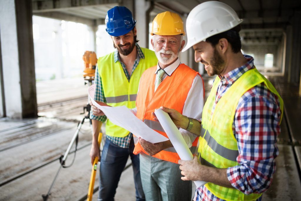 Three construction workers in hard hats reviewing plans at a building site