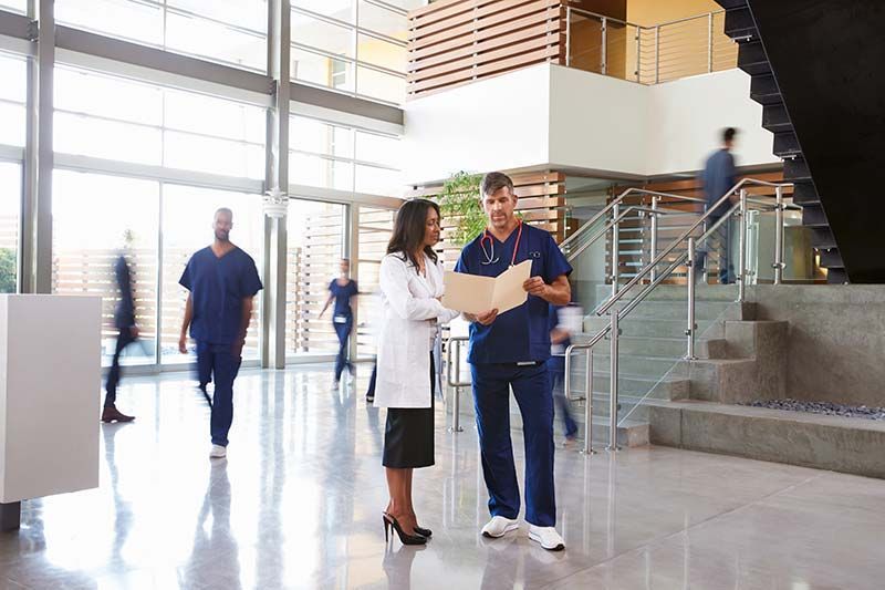 Two coworkers reviewing papers in a bright office lobby near a staircase