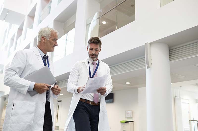 Two doctors in white coats walking and talking in a bright modern hospital hallway