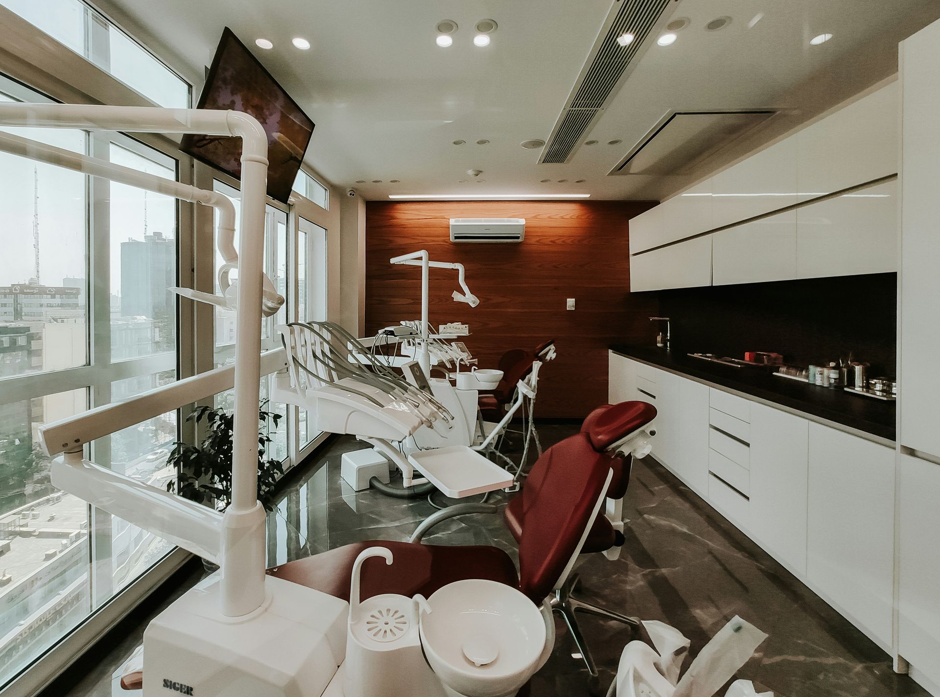 Modern dental clinic with red chairs, treatment equipment, and large windows overlooking a city view