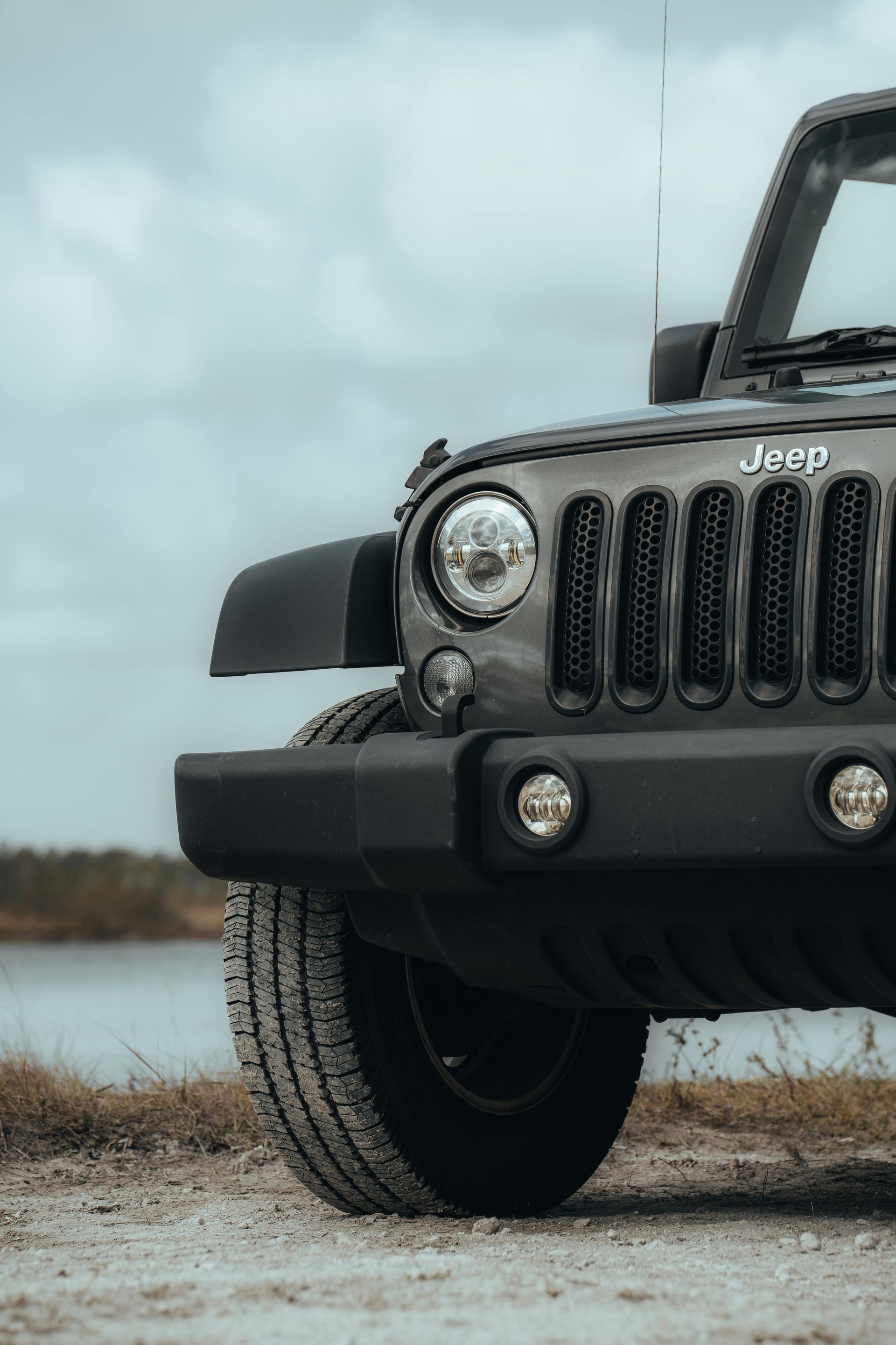 A black jeep is parked on a dirt road next to a body of water.