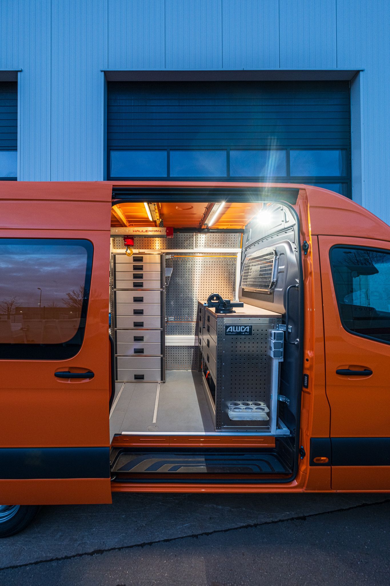 Ein orangefarbener Lieferwagen steht mit offenen Türen vor einem Gebäude.