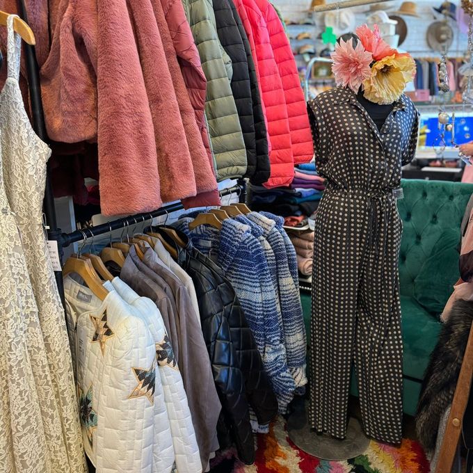 A mannequin wearing a jumpsuit is standing in front of a rack of clothes.