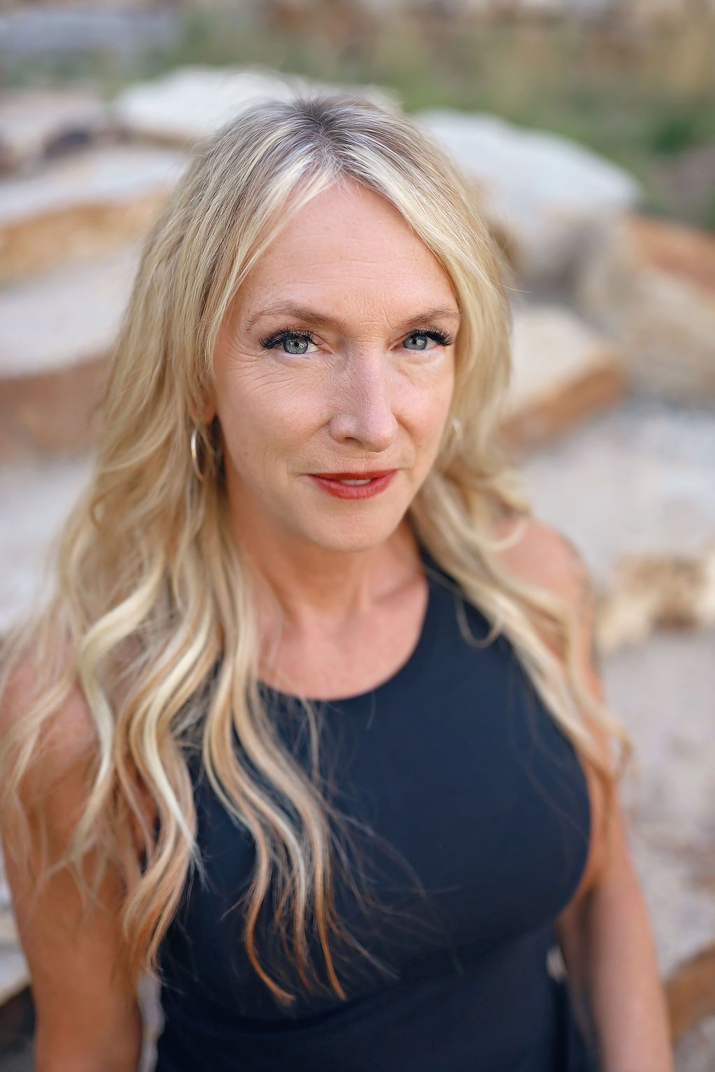 A woman in a black dress is sitting on a bench and looking at the camera.