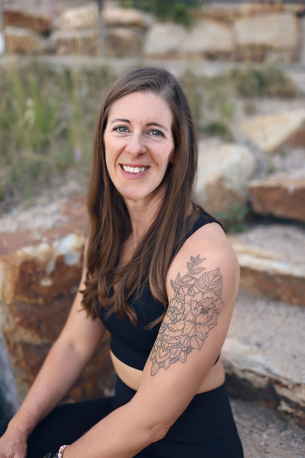 A woman with a tattoo on her arm is sitting on a rock.