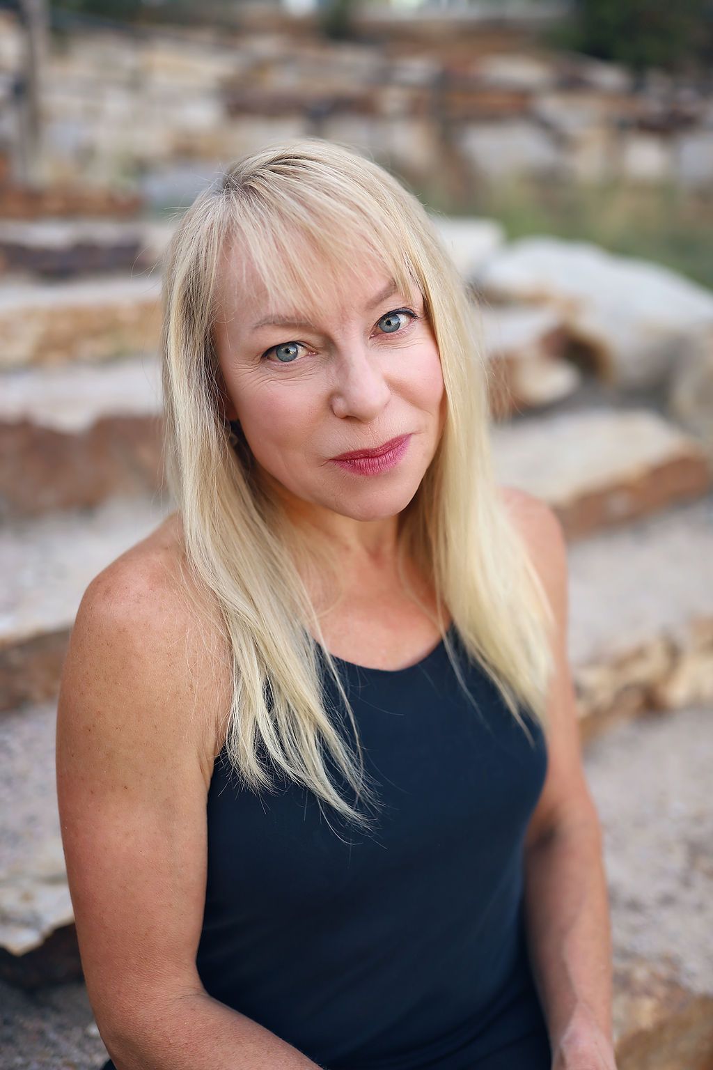 A woman in a black tank top is sitting on a rock.