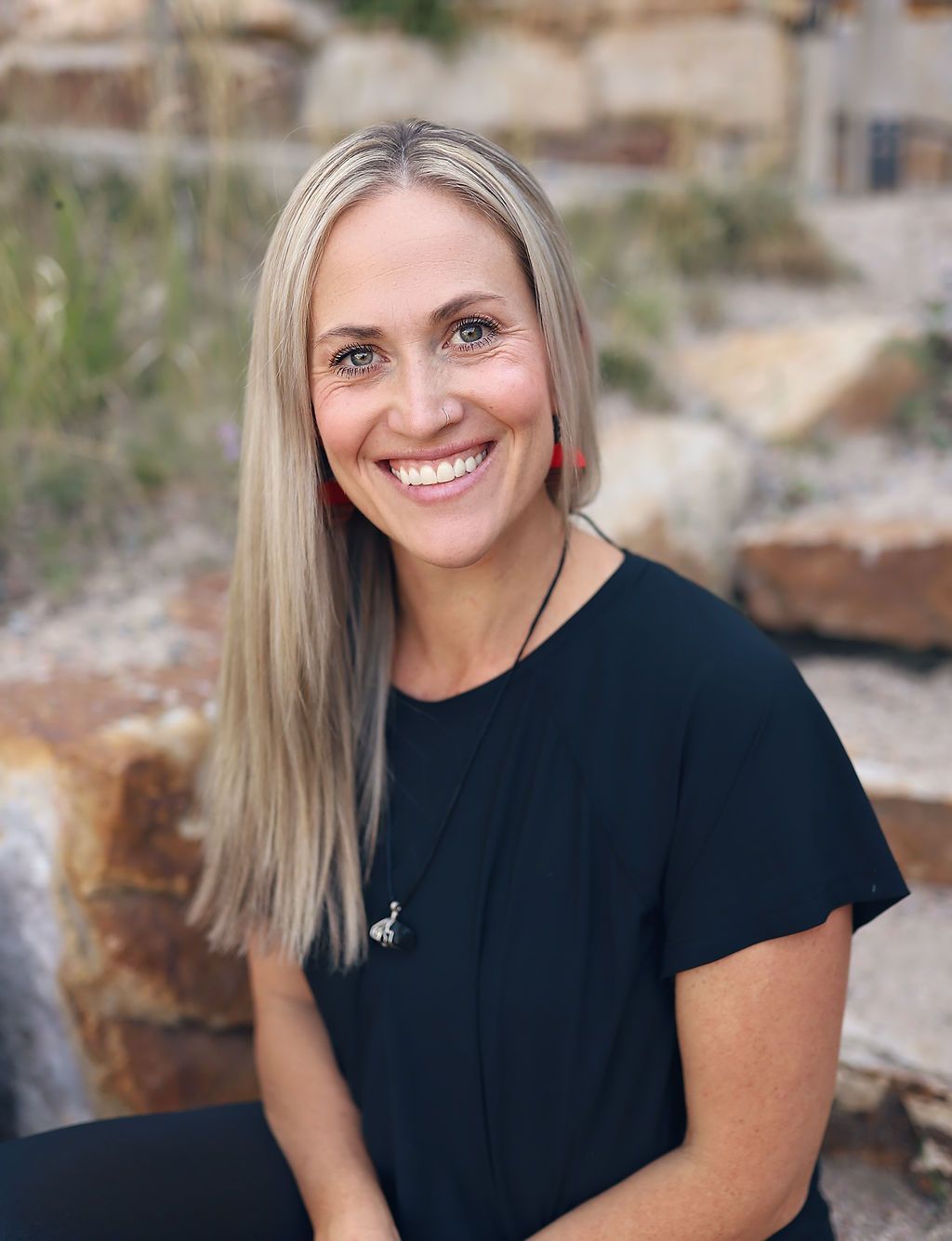 A woman in a black shirt is smiling while sitting on a rock.