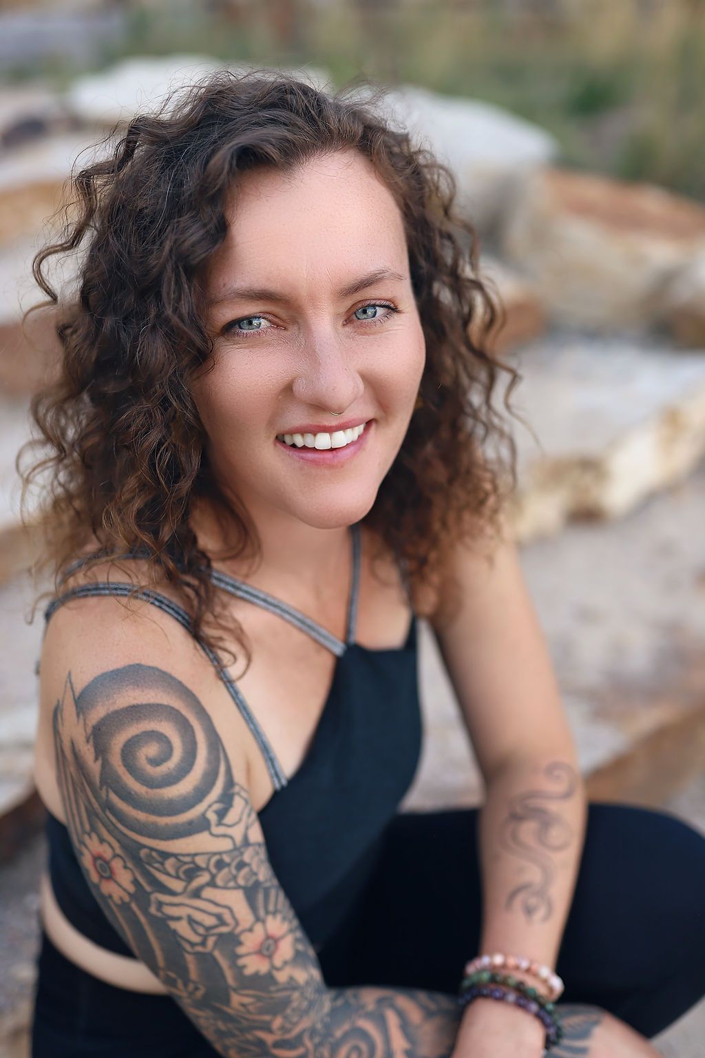 A woman with curly hair and tattoos on her arms is smiling for the camera.