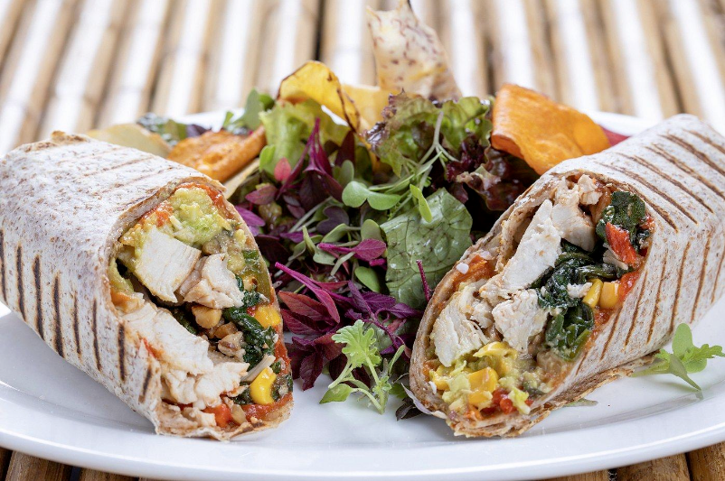 A white plate topped with two wraps and a salad.