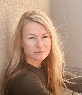 A woman with long blonde hair is leaning against a wall.