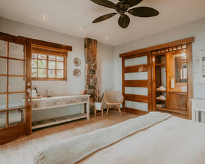 A bedroom with a bed , chair , table and ceiling fan.