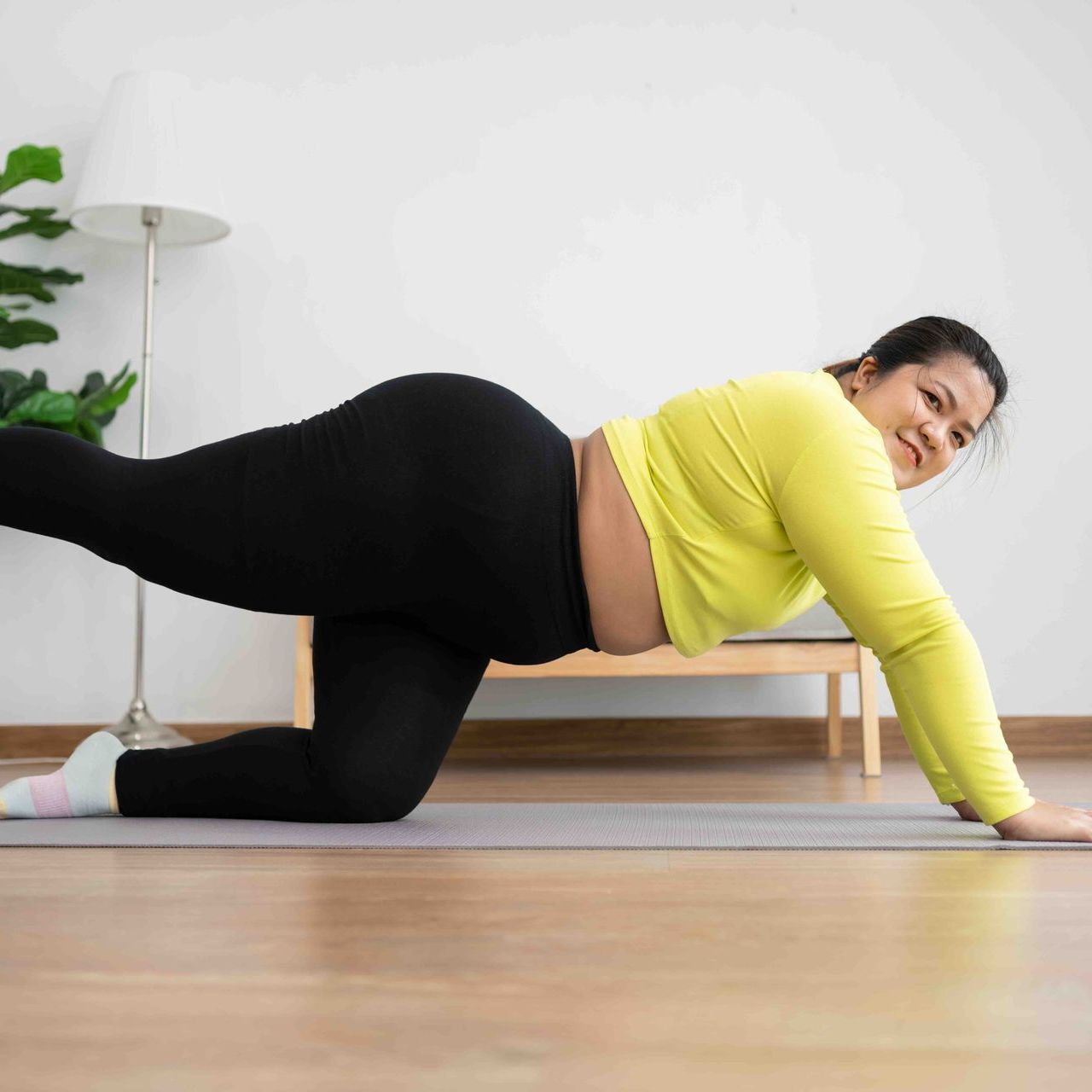A woman is kneeling on a yoga mat in a living room.