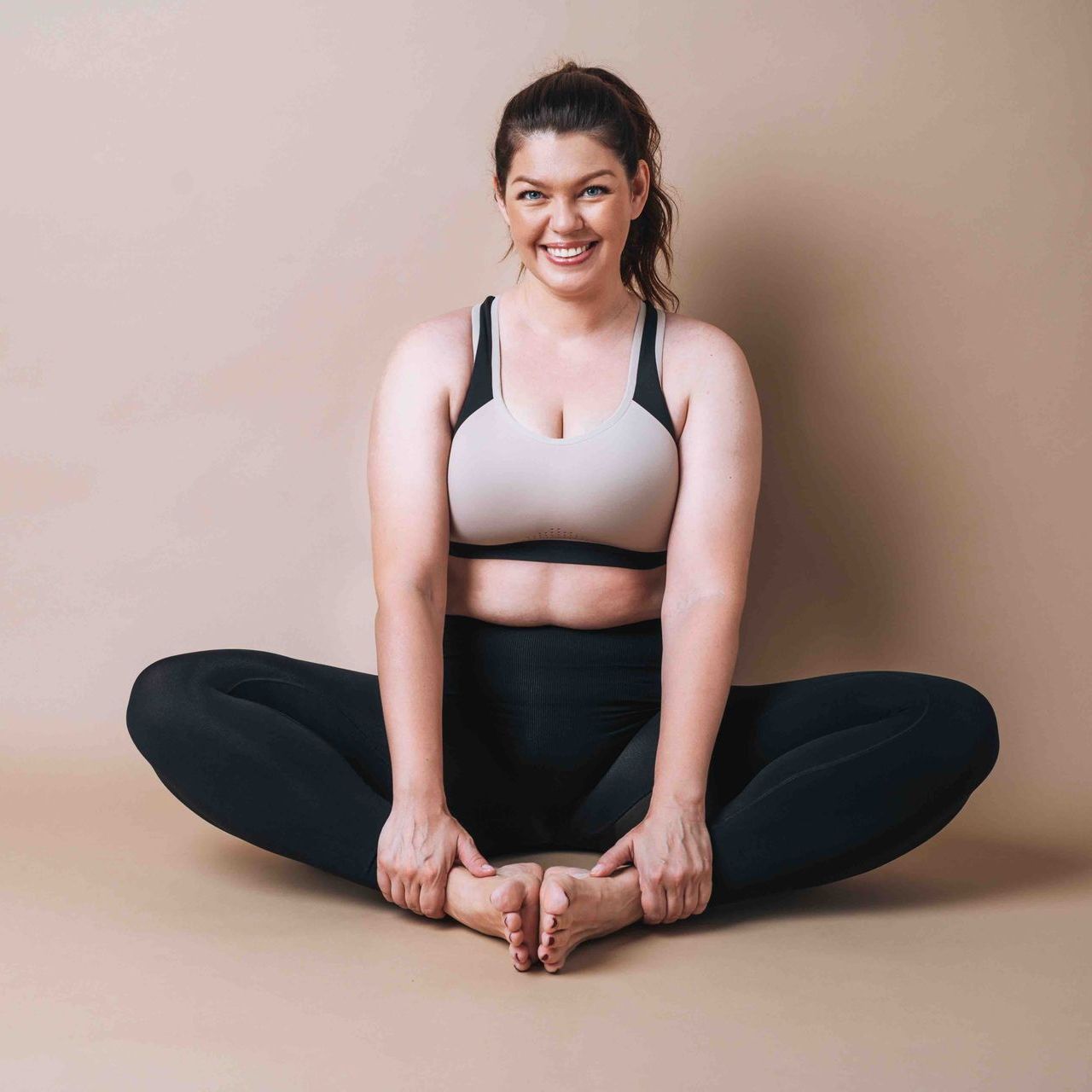 A woman is sitting on the floor with her legs crossed and smiling.