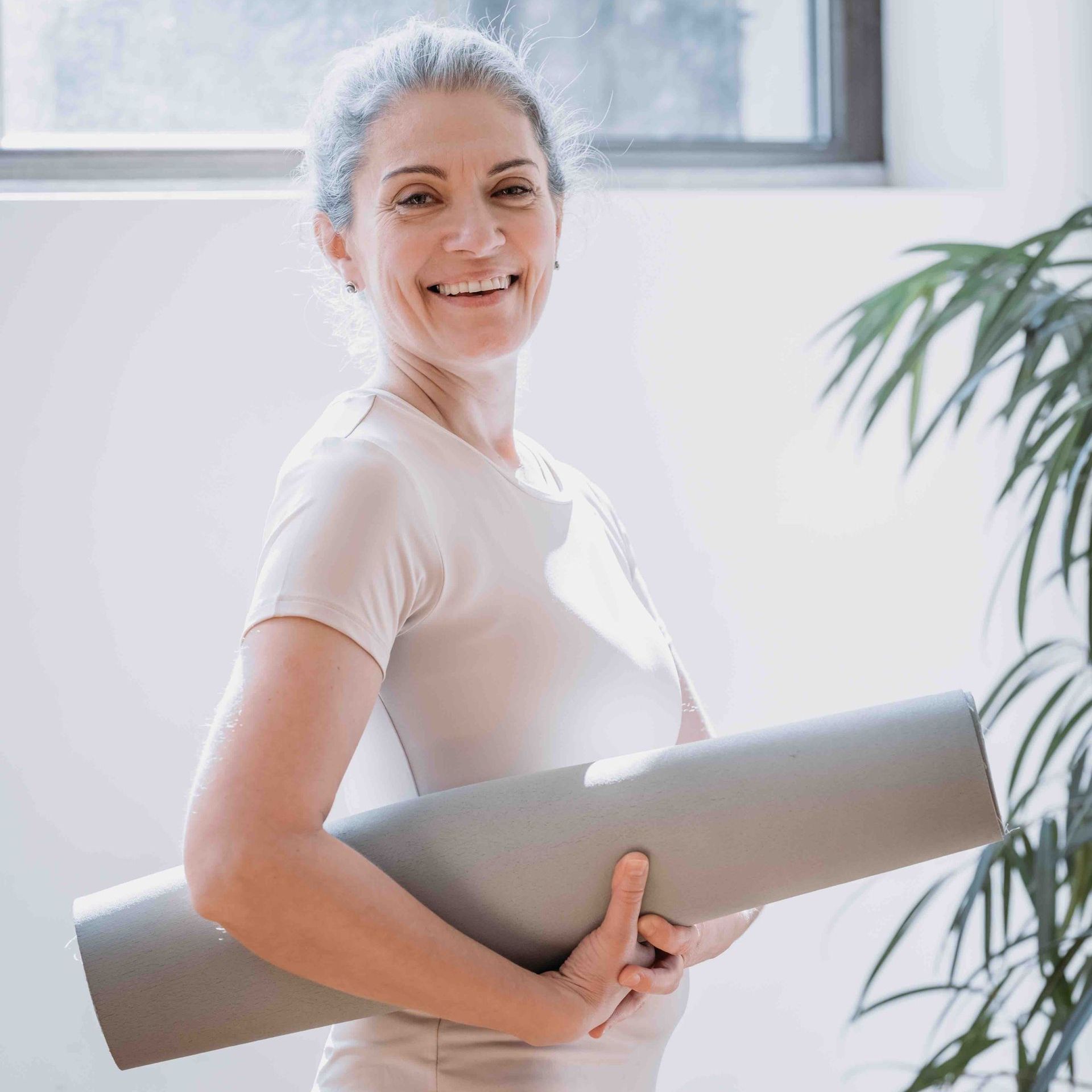 A woman is holding a yoga mat in her hands and smiling.